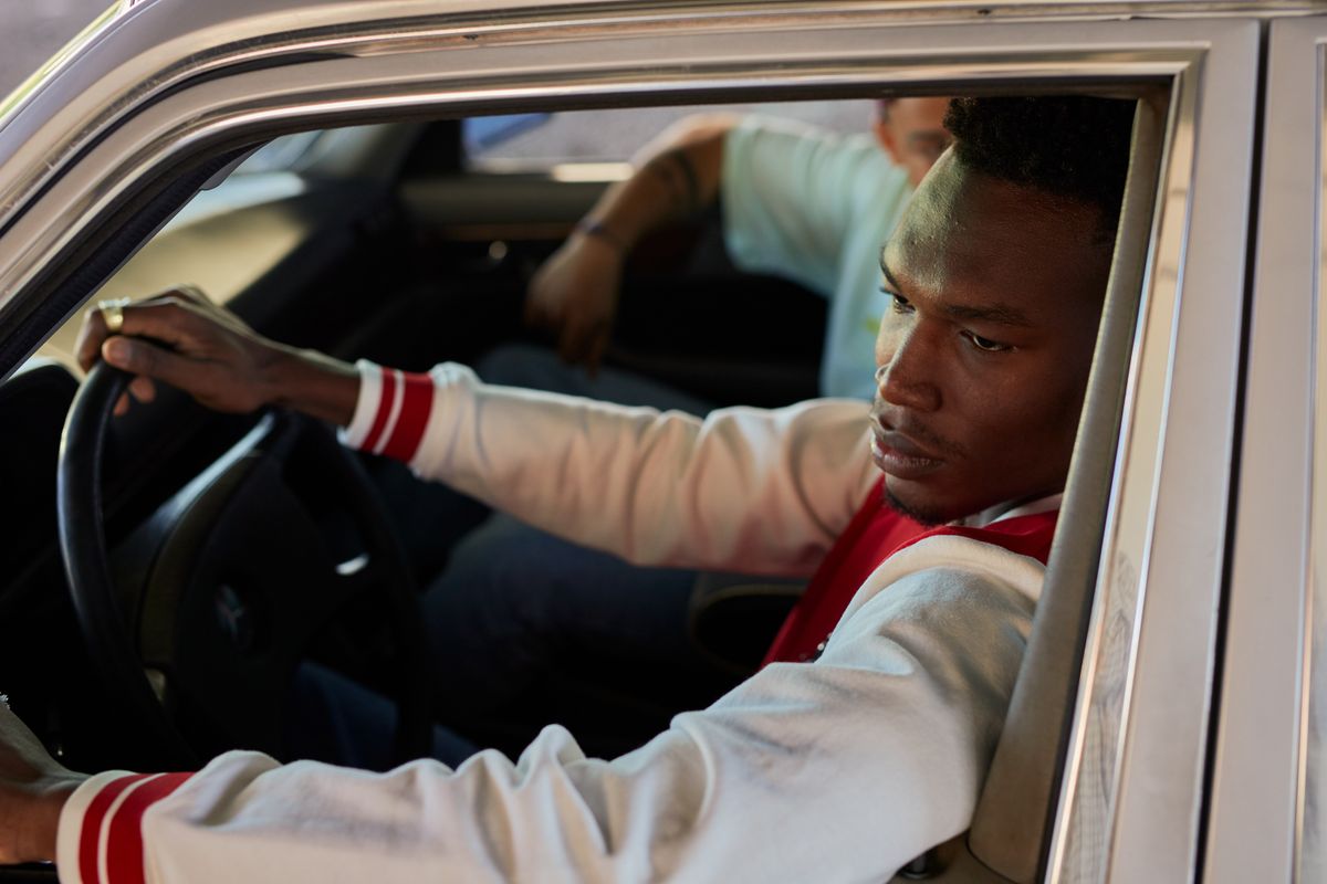 A young man in a varsity jacket driving a car