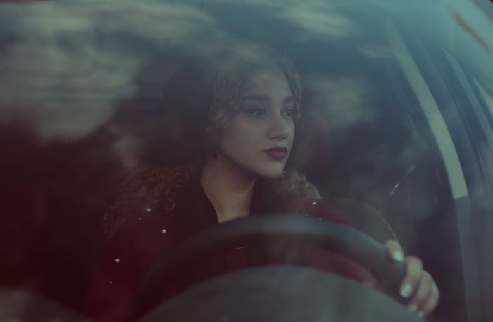 A young woman with curly hair focuses on driving through the city