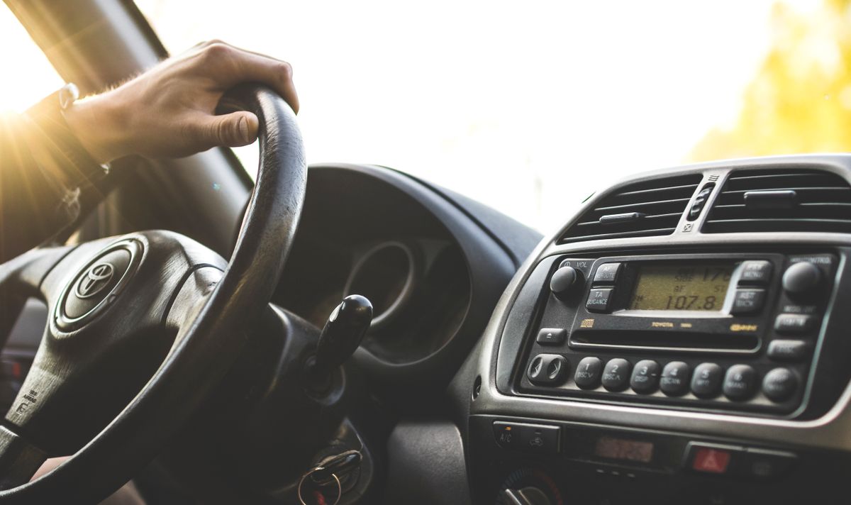 Close-up of a hand on a steering wheel inside a car, dashboard visible