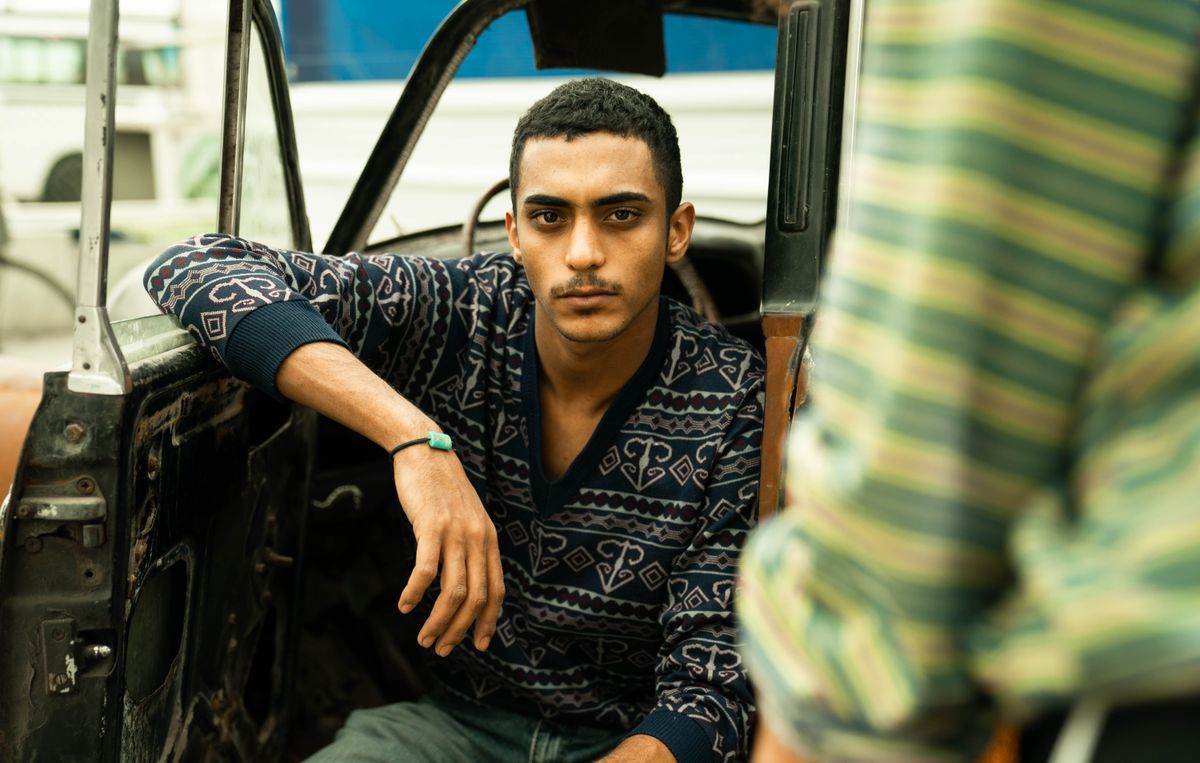 Portrait of a young man sitting inside a car with the door open