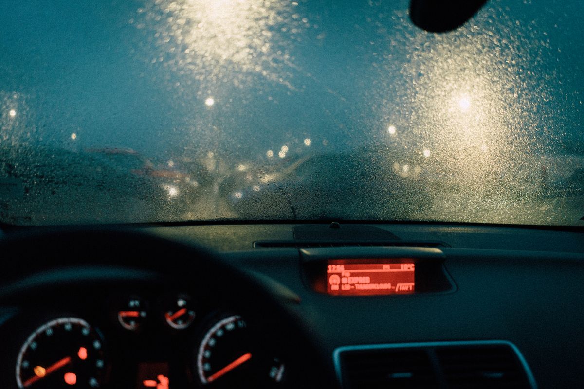 View from car interior with raindrops on windshield and blurred lights at night