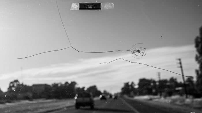 Black and white shot of a cracked windshield, driving on a Buenos Aires road