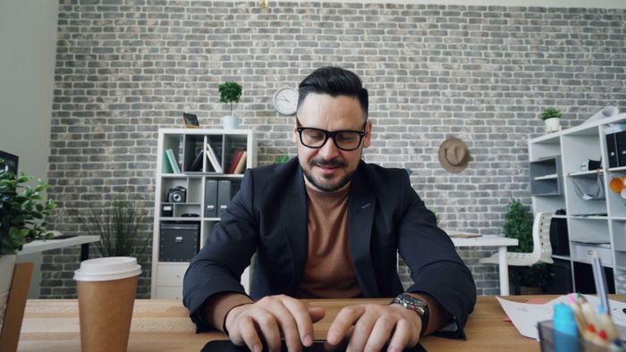 A man in glasses smiles while typing on a laptop in a stylish office