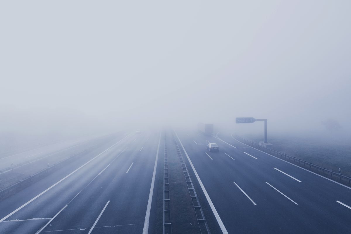 A fog-covered highway with vehicles disappearing into the mist