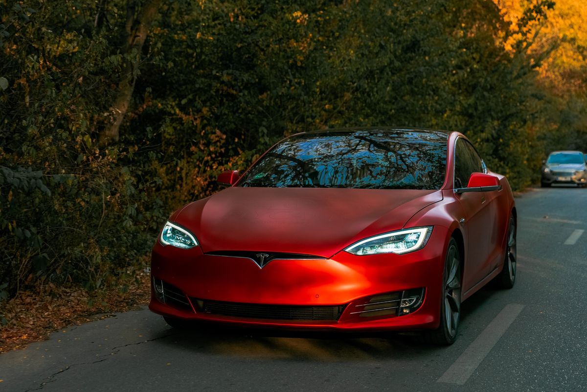 Sleek red electric car driving through a scenic forest road on an autumn day