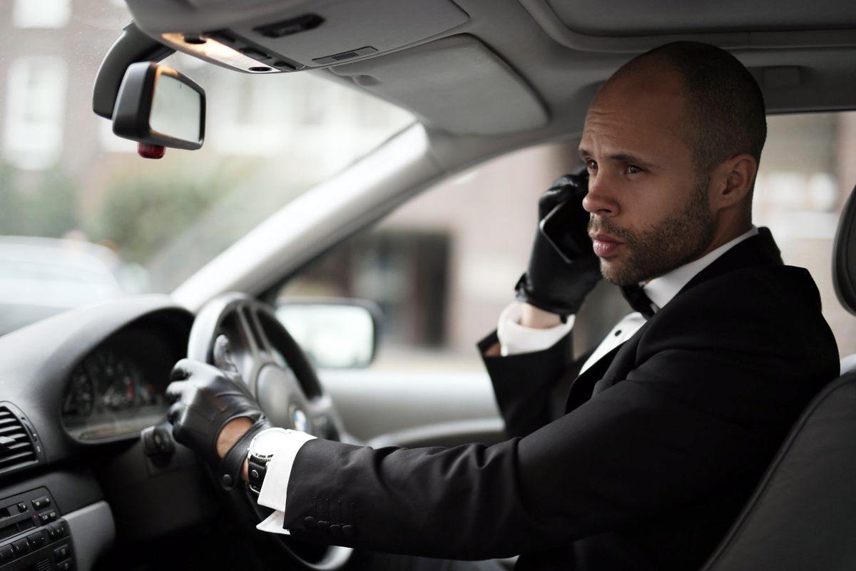 Sophisticated man in suit driving luxury car while on phone call