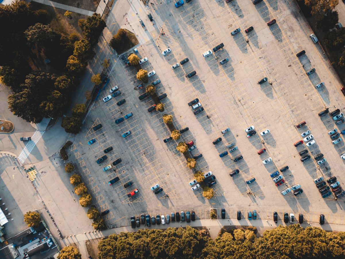 Top-down aerial shot of a parking lot with scattered cars and surrounding trees