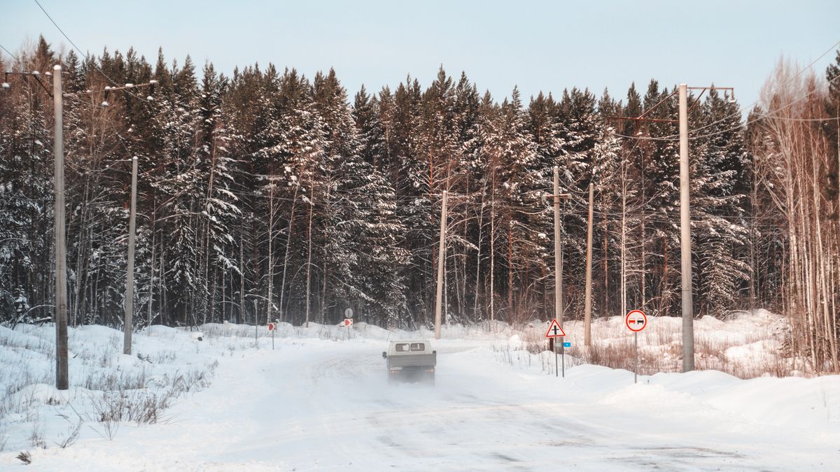 A car drives on a snowy road through a winter forest in Ust-Kut, Russia