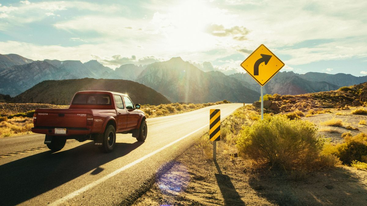 A red pickup truck driving on a sunlit road
