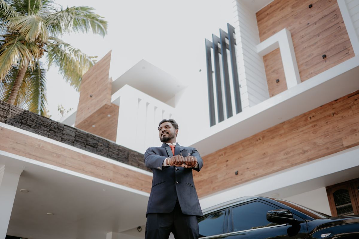 Man in a suit confidently stands beside a black car and modern home exterior