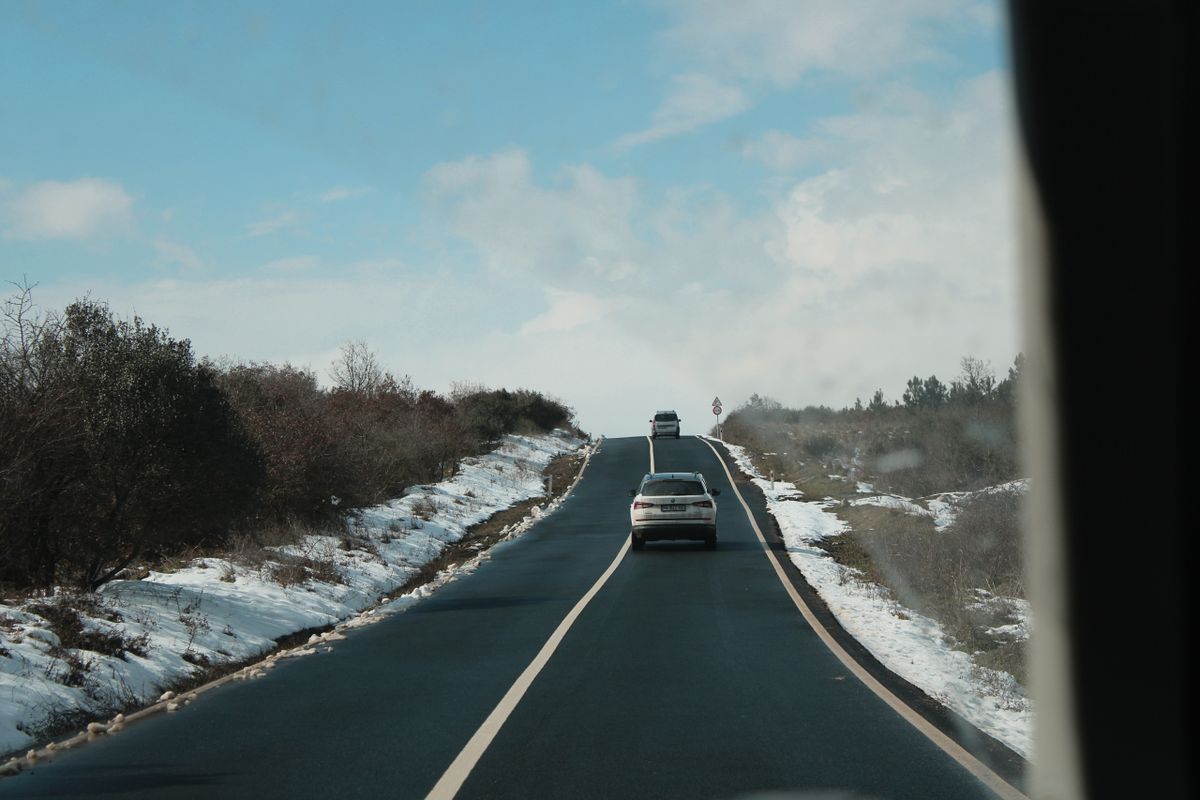 Cars drive along a snowy rural road lined with trees