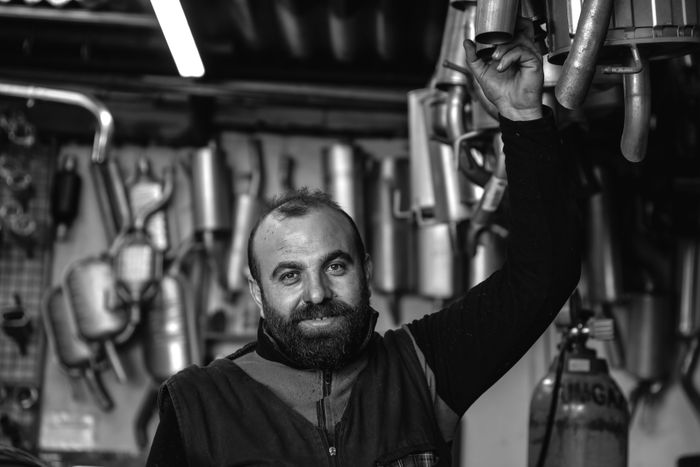 A smiling mechanic holding an exhaust pipe in a car repair garage