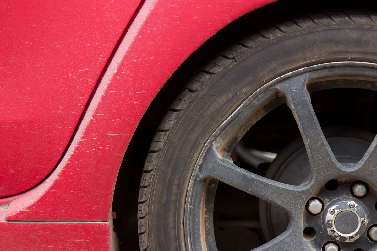 Detailed image of a red car's rusty wheel and tire showing texture and wear