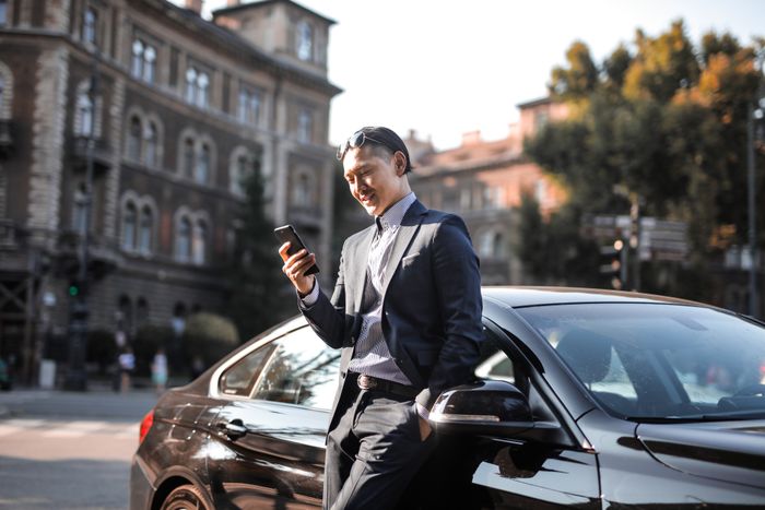 Businessman checking his phone beside a parked car