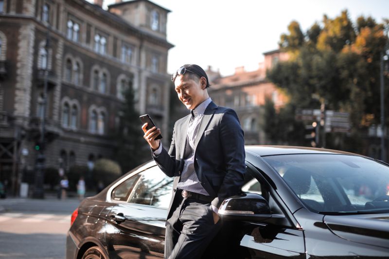 Businessman checking his phone beside a parked car