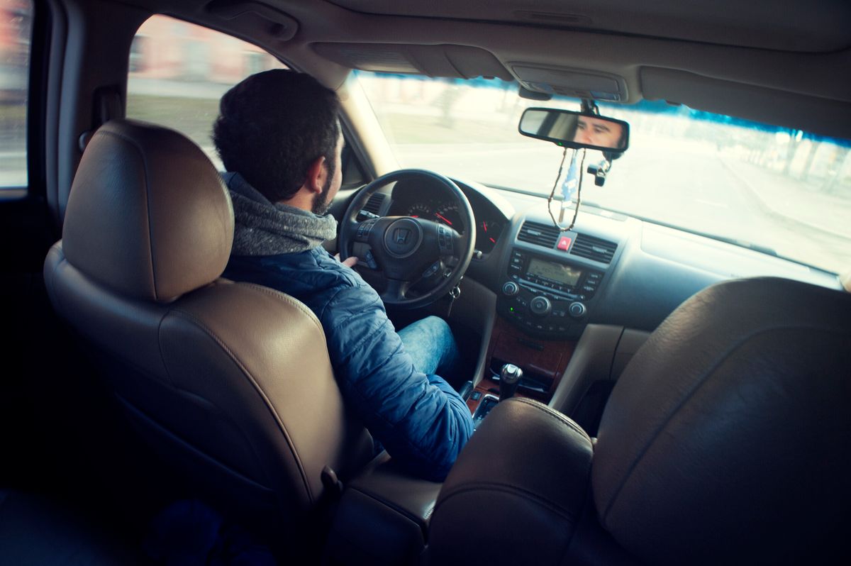 Man wearing blue jacket sitting inside car while driving