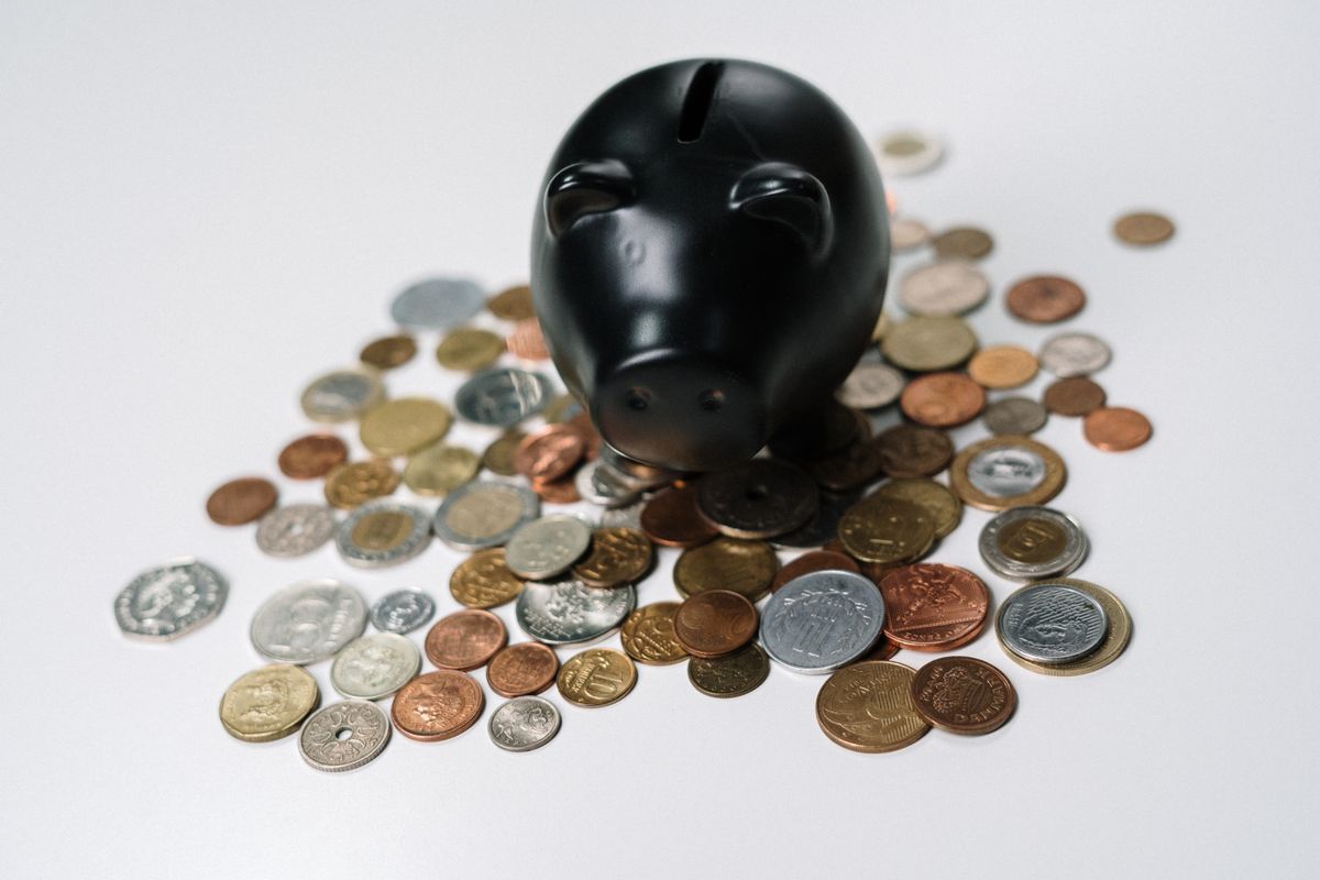 Black piggy bank surrounded by a variety of coins on a white surface
