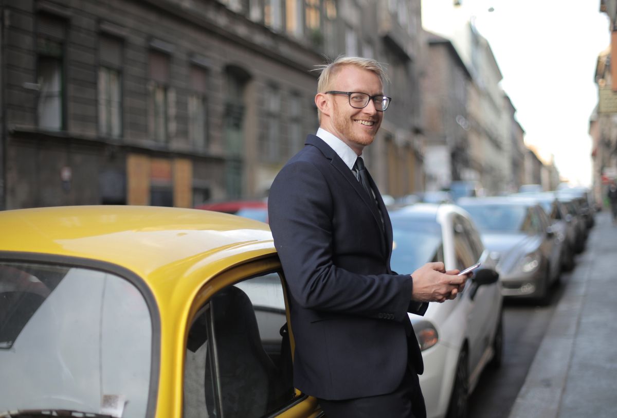 Stylish businessman in formal attire stands confidently by a yellow car