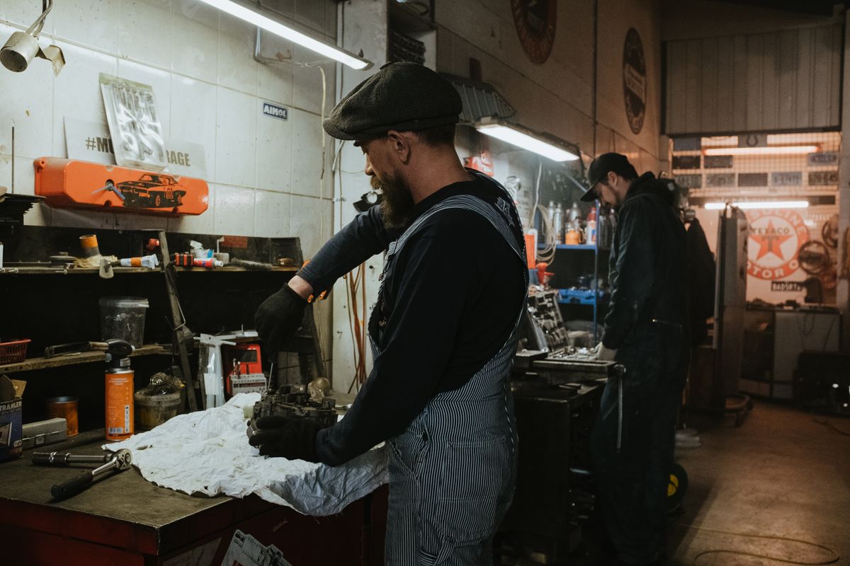 Two auto mechanics engaged in vehicle repair work inside a dimly lit garage