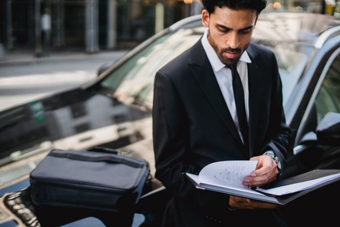 Confident businessman reviewing documents on the street beside a car