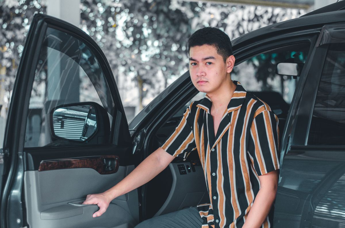 Portrait of a young man with a striped shirt standing beside an open car door