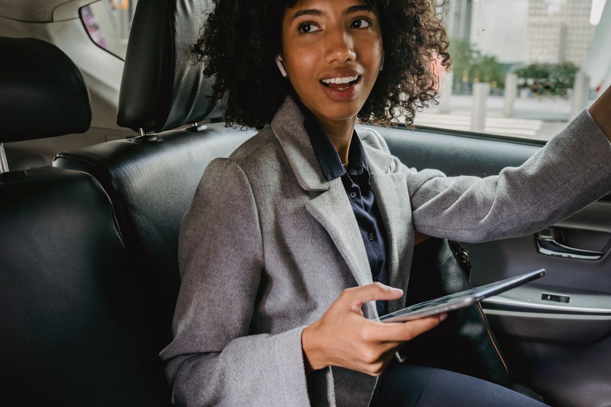Confident woman in business attire smiling while using tablet in a car interior