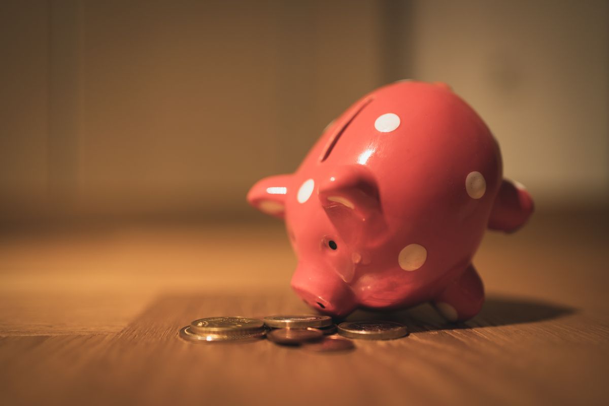 A red ceramic piggy bank with polka dots surrounded by coins