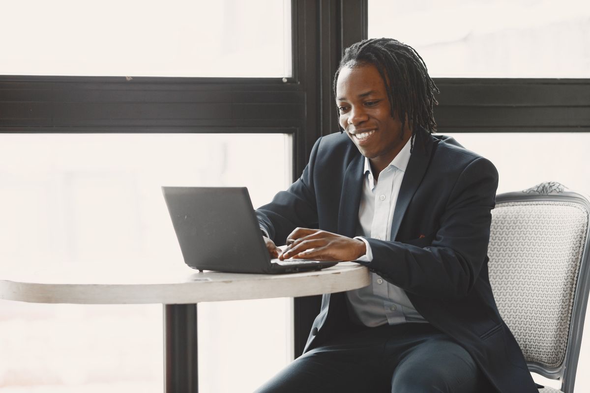 Smiling man in a suit working on a laptop at a table in a modern office setting