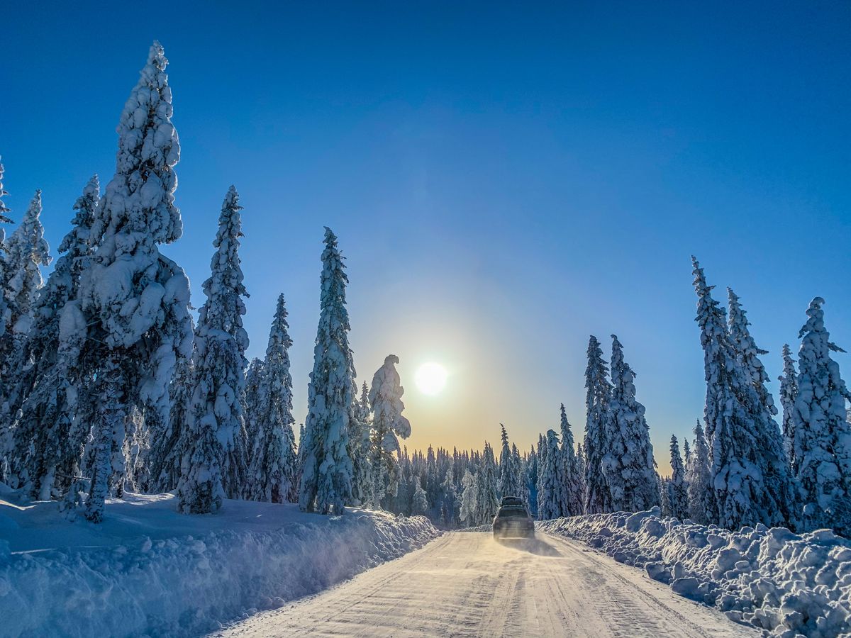 A car drives through a snowy forest under a bright sun in Torsby, Sweden