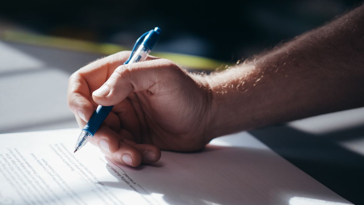 Detailed shot of a hand holding a blue pen while signing a document