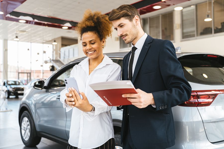 A woman and man smiling while reviewing details at a car dealership