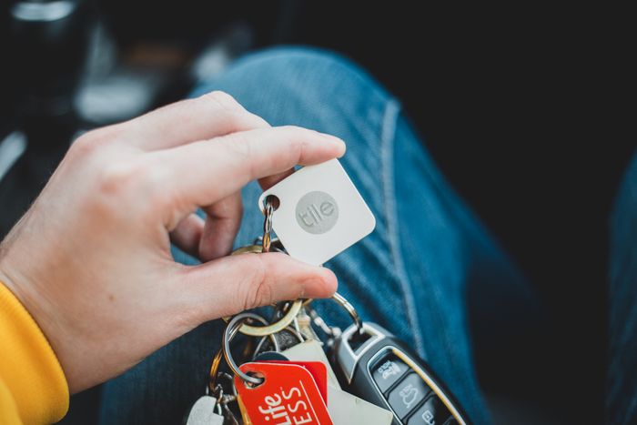 A close-up of a hand holding a set of car keys with various keychains and tags