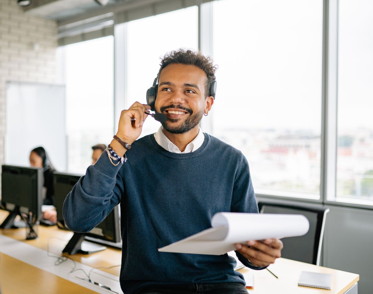 A cheerful man wearing a headset and holding a clipboard