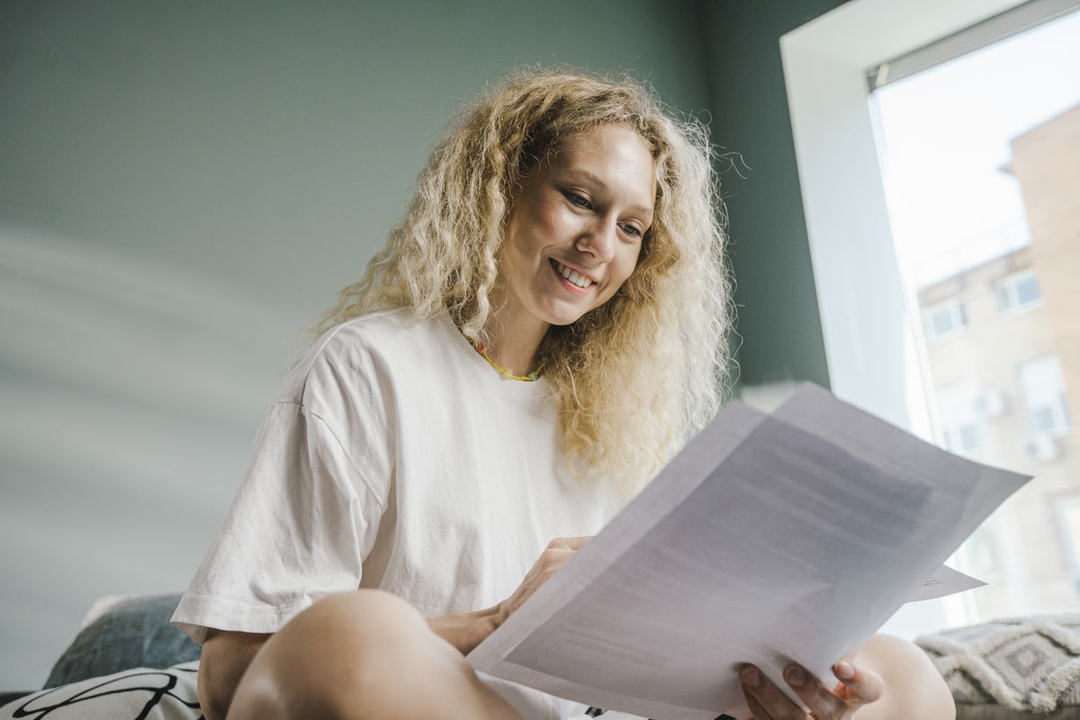 A woman with blonde hair smiling while reviewing documents indoors