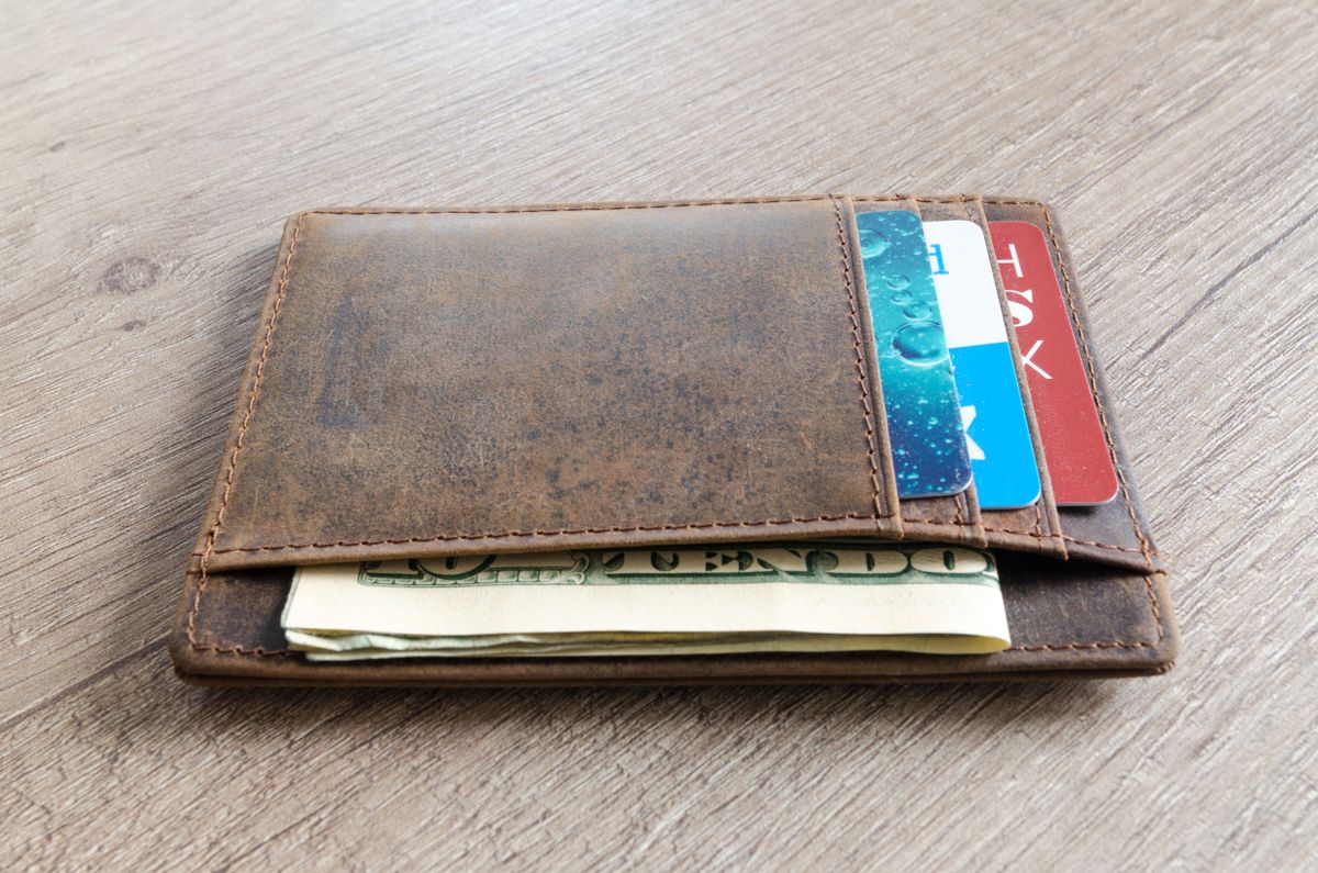 A brown leather wallet with cash and credit cards on a wooden surface