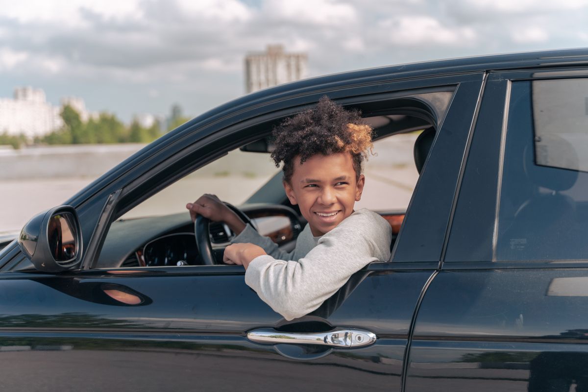 Teenager with curly hair smiling while sitting in car outdoors on a sunny day