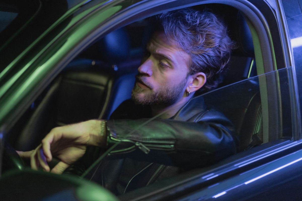 A man with a beard sits in a car seat at night